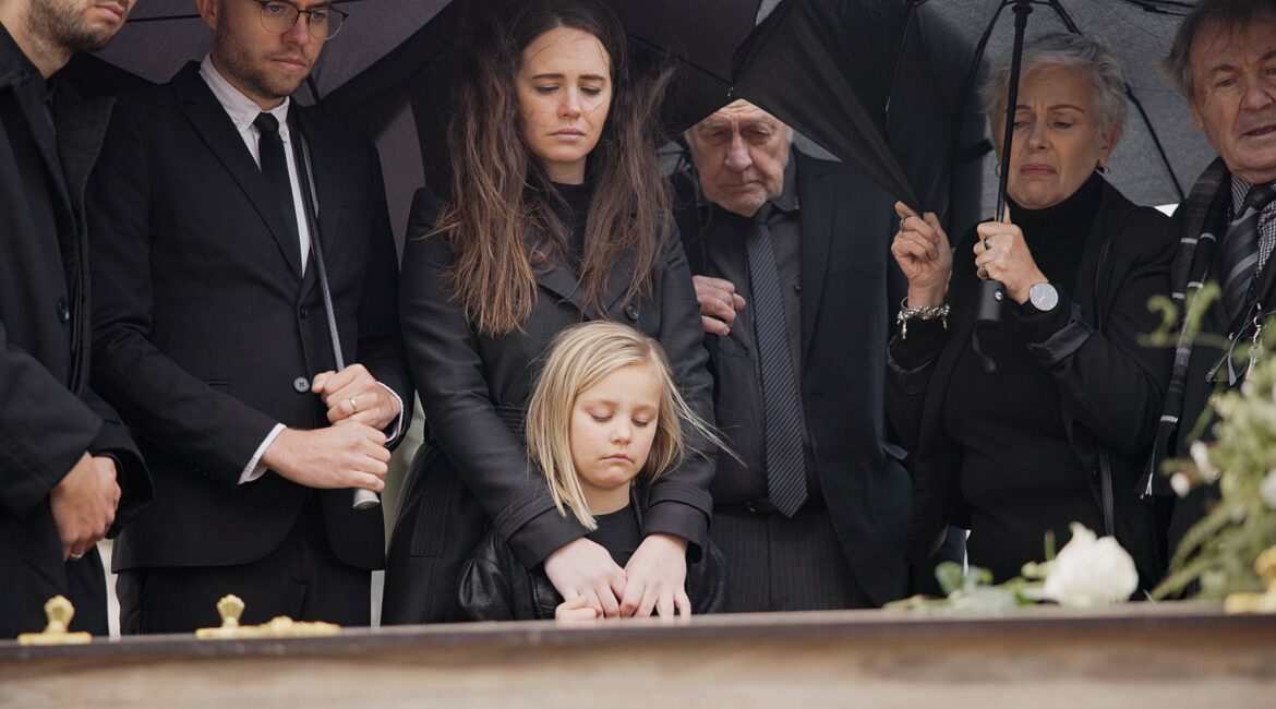 Loss, grief and people at funeral with umbrella, flowers and coffin, family with sad child at servi