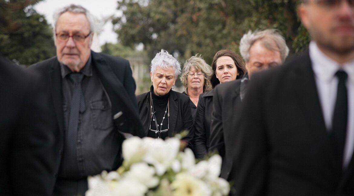 Pallbearers, men and walking with coffin in funeral, ceremony or mourning event at graveyard with s
