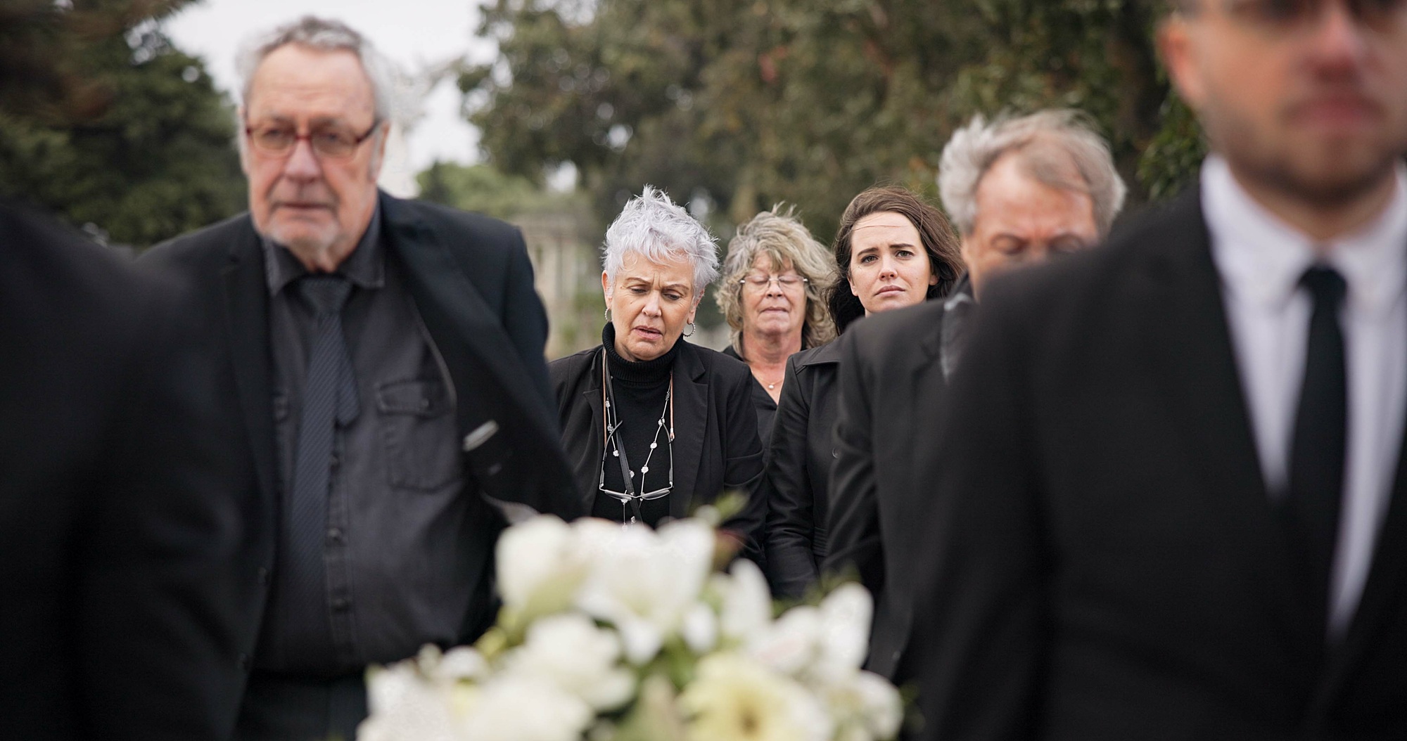 Pallbearers, men and walking with coffin in funeral, ceremony or mourning event at graveyard with s